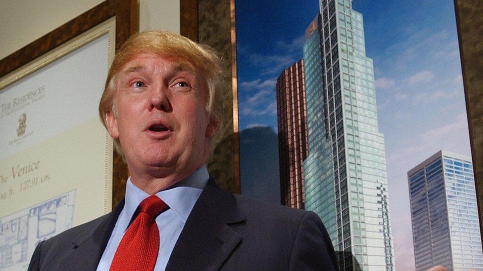 donald trump standing in front of an image of a large skyscraper