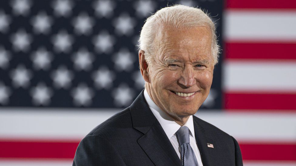 Joe Biden smiling in front of the American flag