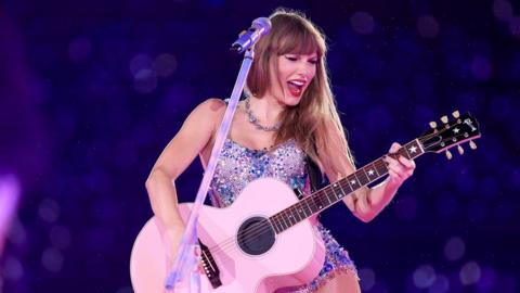 Taylor plays the guitar on stage.