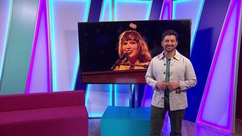 Ricky on the Newsround set with a picture of Taylor Swift