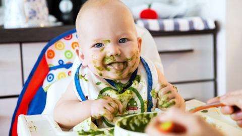 Baby covered in green food smiling.
