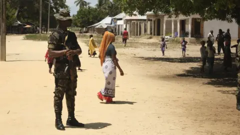 A mozambican soldier looks on as civilians are seen in Quionga, Mozambique, on September 30, 2022. - In March 2021, fighters affiliated to the Islamic State group attacked the port city of Palma -- the jewel in the crown of a gas project that would supposedly shower Cabo Delgado province with good jobs and desperately-needed infrastructure.