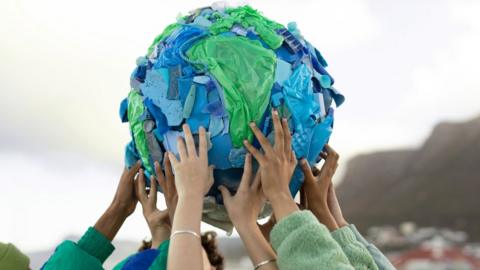 hands holding up a planet made out of recycled plastic