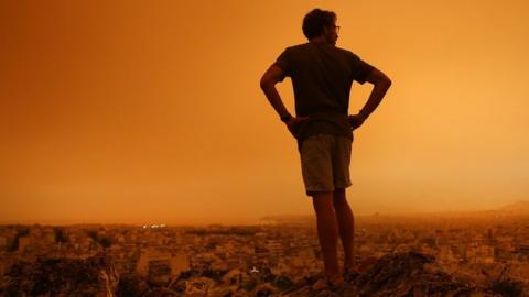 man-staring-at-orange-dust-storm-in-athens.