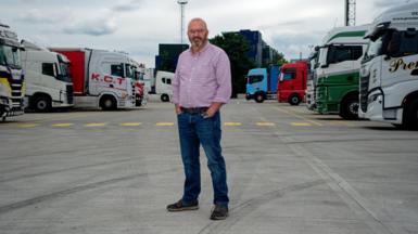 Matt Dangerfield standing in the truckstops with a number of lorries parked up either side of him