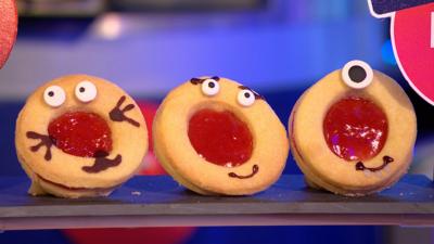 Three biscuits with circular jam centres are decorated with edible googly eyes and smiley faces.