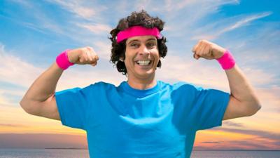 Andy Day wearing a blue t-shirt with a pink sweatband on his head and one on each wrist.