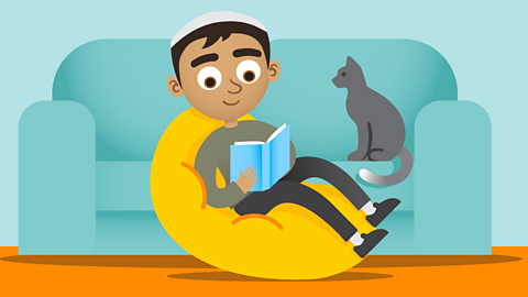 Boy sat on beanbag reading whilst his cat looks on.