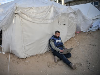 Un periodista sentado junto a una tienda de campaña mientras intenta conectarse a internet en Rafah, Gaza