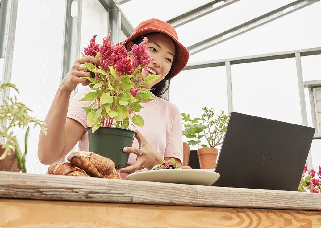 Žena ošetruje rastlinu a pozerá sa na prenosný počítač