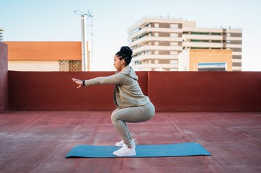 fit person wearing a matching workout set in sage green and wearing a bun does a squat during a lower-body body-weight workout