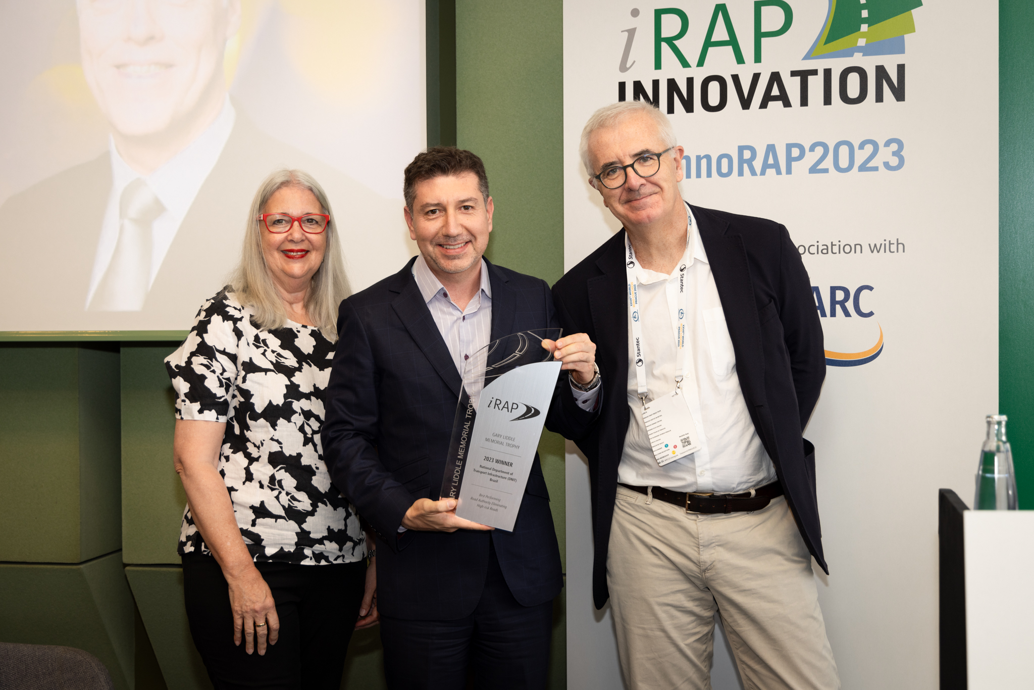Julio Urzua, iRAP Strategic Projects Director accepts the Winner Trophy on behalf of DNIT -with Mrs Meredith Liddle and Miquel Nadal, iRAP Board Chairman