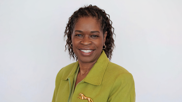 A Black woman wearing a blazer smiles at the camera