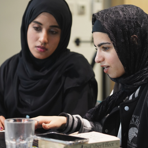 Two women in hijabs work together on a laptop
