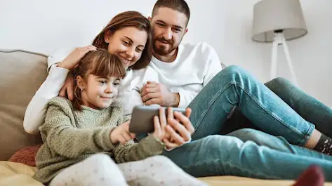 Un père, une mère et une fille regardant une émission de discovery+ sur un téléphone intelligent.