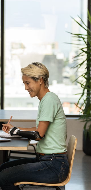 Una mujer con un brazo ortopédico trabaja sentada con su laptop en una oficina.