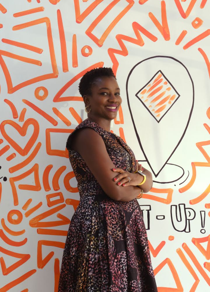 Portrait of Adenike Adeyemi standing in front of a wall painted with orange lines and doodles of hearts
