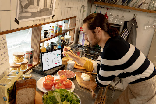 A home cook leans on a kitchen counter to use his tablet with a stylus. He’s surrounded by ingredients and wears a black and white horizontal striped top.