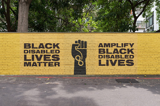 A yellow brick wall painted with the phrases "Black disabled lives matter" and "amplify black disables lives" in black.