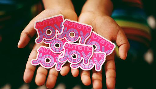 Custom stickers in pink and lavender that read "Austistic Joy"