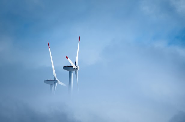 White wind turbines on a cloudy day. They are partially obscured due to the clouds sweeping low past them.