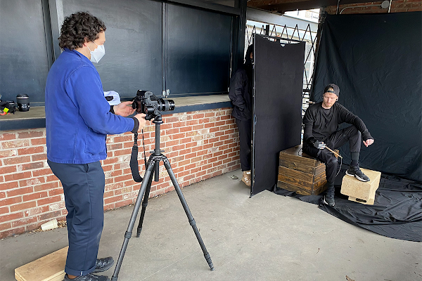 A behind the scenes photo of Justin Kaneps taking a portrait of Jason Barnes. Jason poses against a black backdrop.