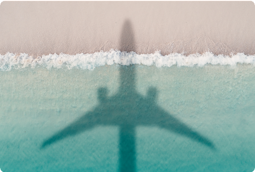 Birds-eye view of a shadow of an airplane on a seashore above waves.