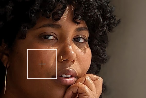 Una mujer afrodescendiente mirando a cámara con un signo de más sobre su color de piel, que ilustra la Escala Monk de Tonos de Piel.
