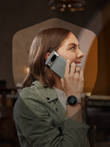 Một người dùng Android mỉm cười khi trả lời điện thoại một cách an toàn và cho thấy chiếc Pixel Watch 2. Bao quanh người này là một khung hình khiên.