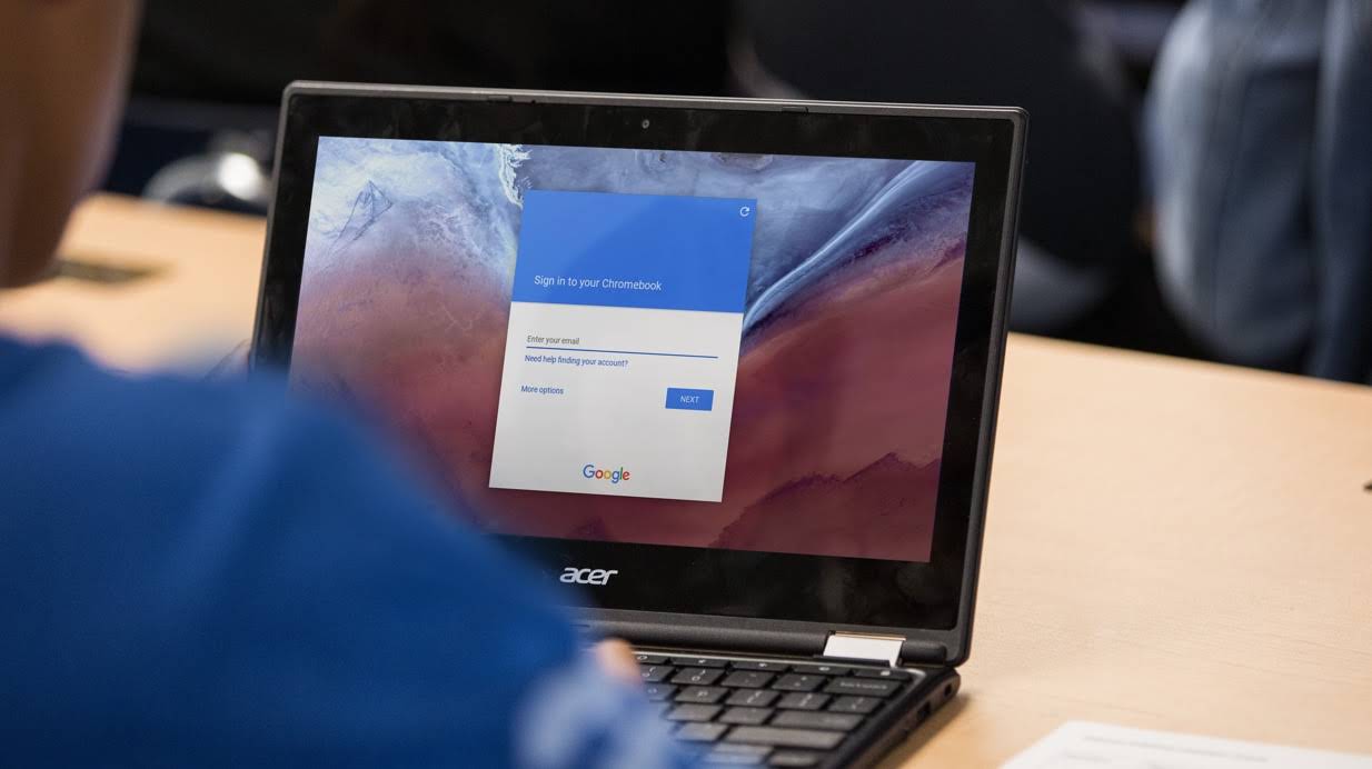 En beskuren bild på en elev som sitter vid ett skrivbord och använder en Chromebook på vilken Googles inloggningsskärm visas.