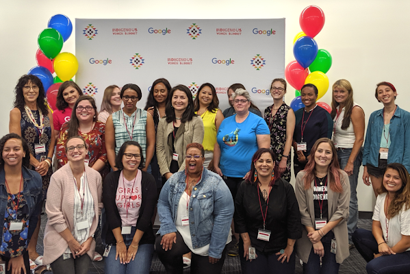 A group of Googlers smile for a photo in front of a large poster board that reads "Indigenous Women's Summit"
