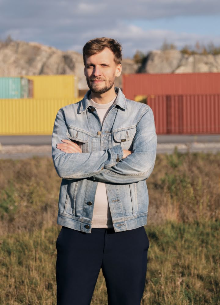 Photograph of Kristian Rönn standing with the sun shining on him, in front of a cargo train that's been painted yellow and red.