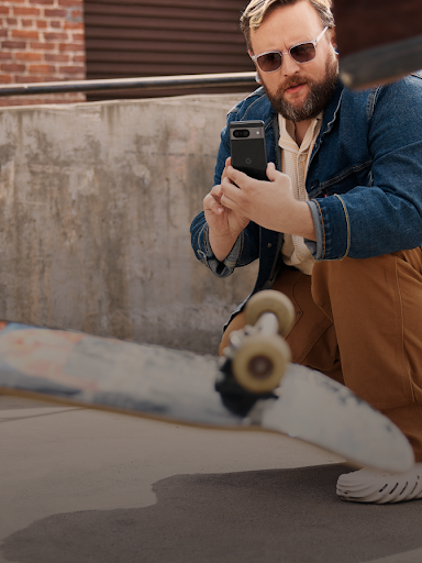 Một người dùng Android ngồi xổm và quay video một người trượt ván đang thực hiện một kỹ thuật.