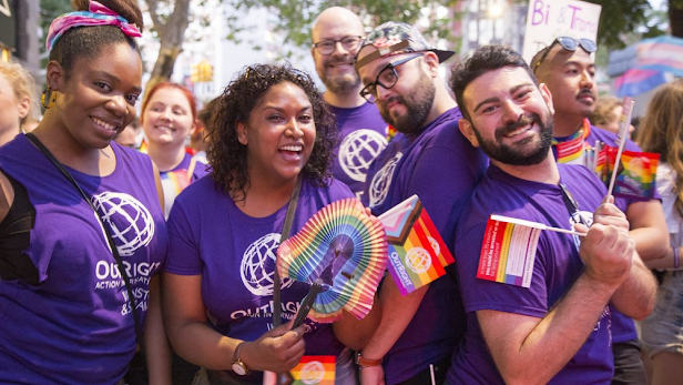 A group of Googlers wear purple shirts and carry rainbow flags at a parade