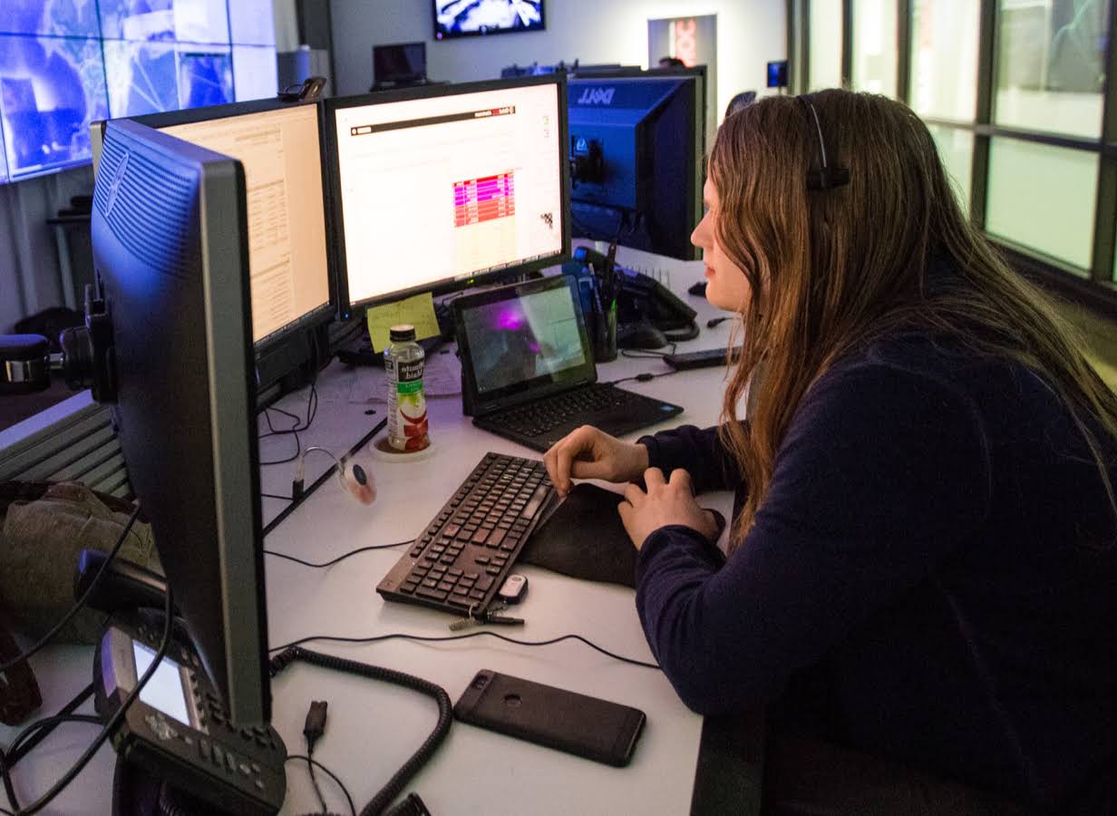 Una mujer joven trabaja en un escritorio frente a tres monitores.