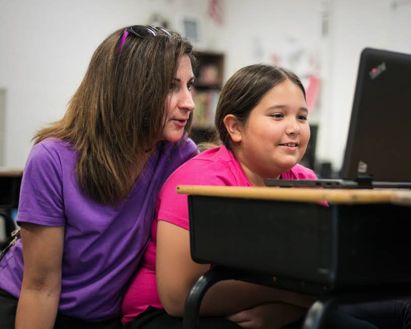A teacher is looking at a Chromebook screen with a young female student.