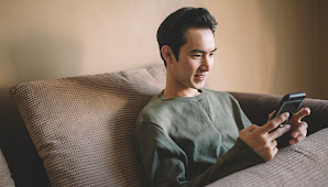 Young man sits on couch looking at cell phone