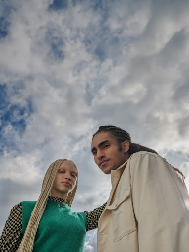 Two people posed next to each other and photographed from the waist up with a blue sky as the background.