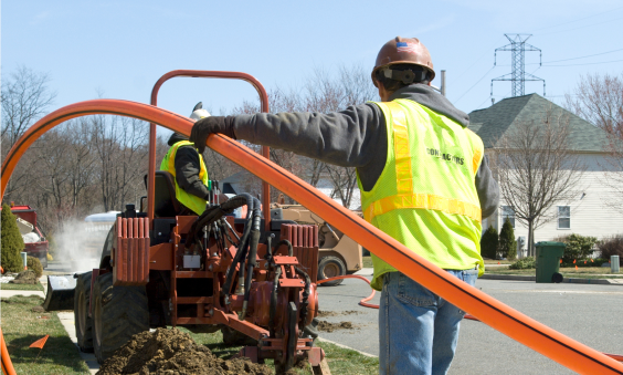 Two construction workers at a telecom operation site in West Des Moines burying the fiber cable using their machine.