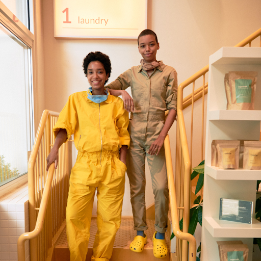 Dos mujeres afrodescendientes paradas en los escalones de su negocio de lavandería sostenible