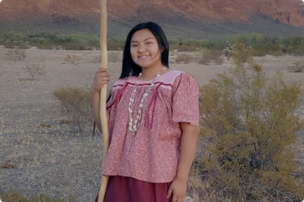 A young Indigenous girl wearing a pink blouse and skirt stands on the Tohono O'odham Nation Reservation