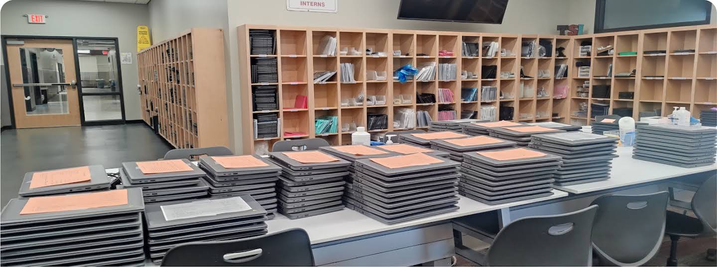 Multiple stacks of repaired Chromebooks are resting on desks, waiting to be handed out to students.