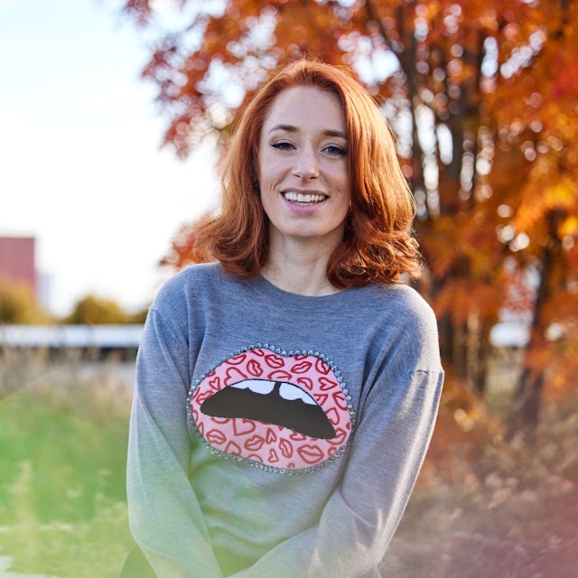 Professor Hannah Fry posing outdoors. It's autumn – a tree in the background's leaves have turned golden brown.