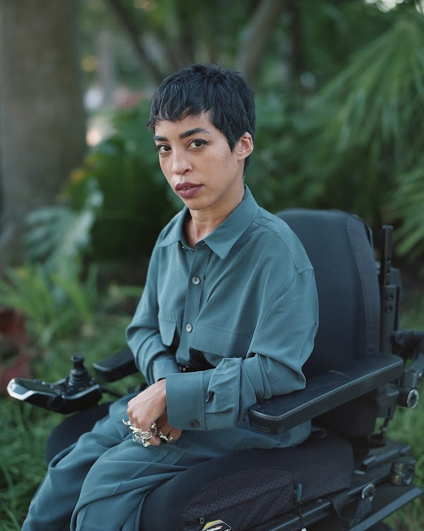 Jillian Mercado, founder of Disabled Black Creatives in their wheelchair wearing a teal silk shirt.