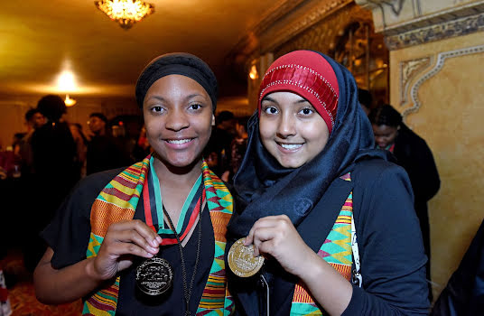 Two young women with colorful scarves holding up medals.