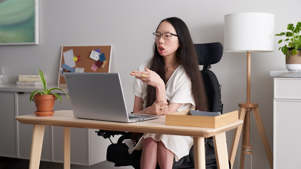 Googler Aubrie Lee (she/her) sits in her wheelchair and takes a meeting at a desk