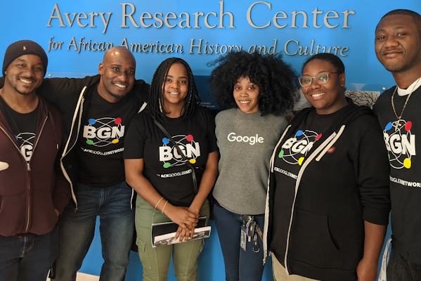 Six Black Googlers wear Google branded apparel and smile at the camera