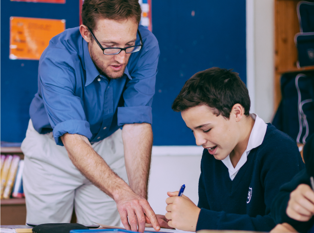 A teacher watches over as a student completes an assignment.