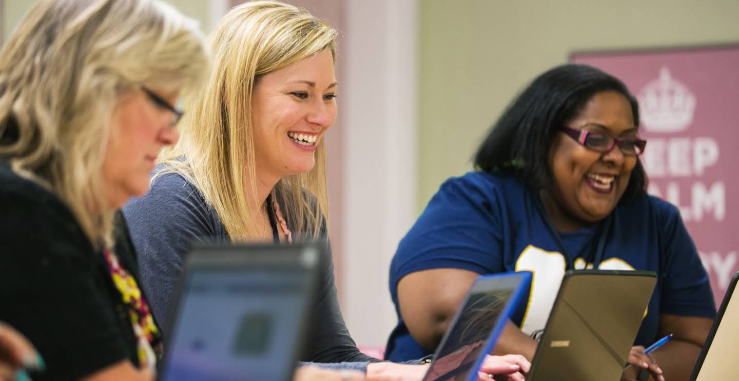 Three female educators smiling in front of their laptops.