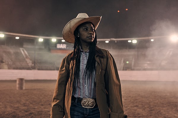Keiara gazing across a brightly lit arena at night in her rodeo garb.